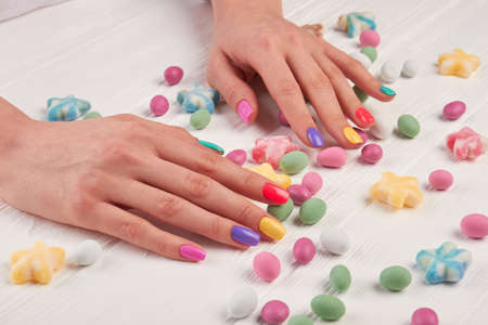 Girls manicured hands and sweets. Girls hands polished with different colors and colorful candies on...
