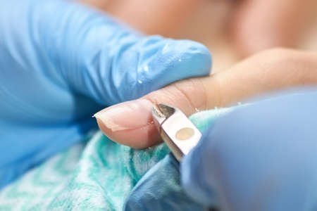 Manicurist cut the cuticle to the client. Nail beautician cutting the cuticle using cuticle scissors. Manicure and skincare.の写真素材