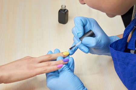 Woman having nail manicure in beauty salon. Manicurist painting nails to client with different...