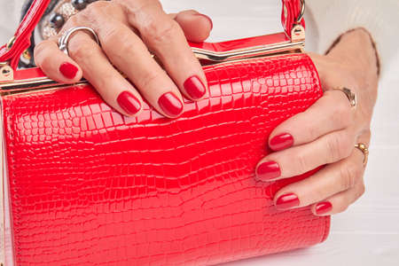Luxury red handbag in female manicured hands. Aged woman hands holding beautiful leather bag close up. Female fashionable accessory. Female trendy manicure.の写真素材