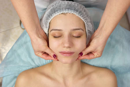 Facial massage young woman. Hands of beautician, female face.