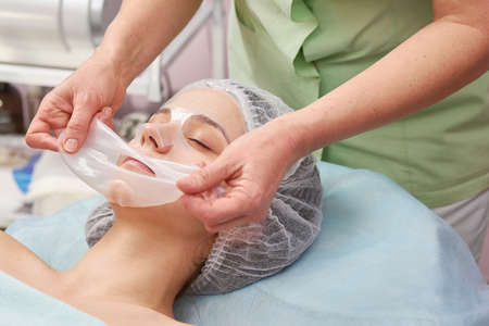 Cosmetician applying facial hydrogel mask. Customer of cosmetology clinic.