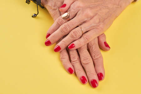 Female hands with beautiful red manicure. Senior woman hands with red nails polish on yellow salon table. Nail salon and spa.の写真素材