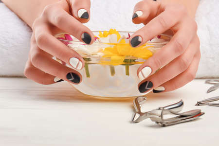 Female hands on manicure bath. Woman hands with stylish manicure on bowl with chrysanthemums, manicure tools.の写真素材