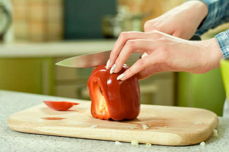Hands of woman cutting paprika. Red bell pepper, wooden board.