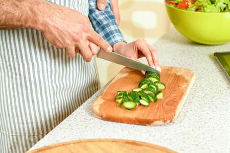 Hands of couple cooking. Pieces of cucumber on board. Love and health.の写真素材