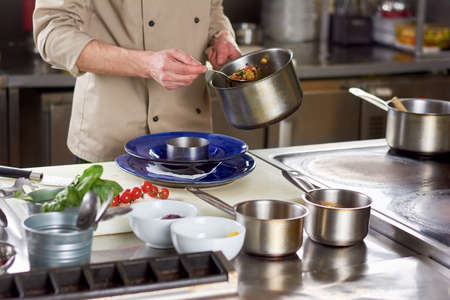 Chef put out with spoon stewing vegetables. Cropped image of male chef going putting garnishing into...