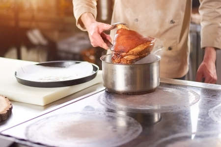 Chef holding large piece of lab leg. Male chef at professional kitchen putting out lamb shank from saucepan.の写真素材