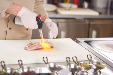 Chef hands with torch burner. Torch blowing fire on meat. Chef is preparing duck breast.の写真素材
