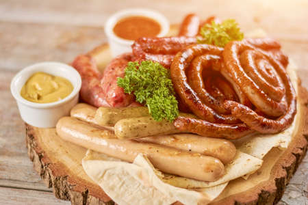 Tasty grilled sausages on wooden board. Assortment of grilled sausages served with parsley. Delicious german food.の写真素材