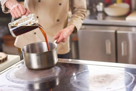 Chef pouring brown liquid in saucepan. Male chef cooking a broth for lamb shank boiling. Chef at professional kitchen.の写真素材