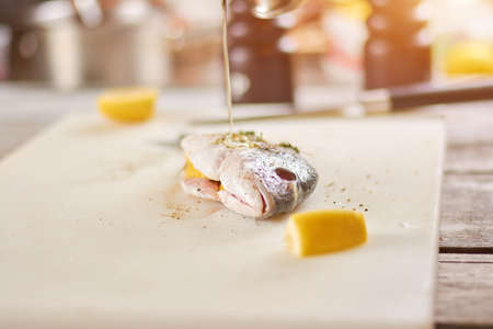 Pouring with oil the raw fish. The process of cooking dorado fish close up. Seafood restaurant and marine products.の写真素材