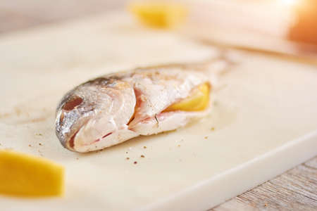 Raw fish prepared with salt and spices. Raw fish with lemon inside on kitchen board close up....