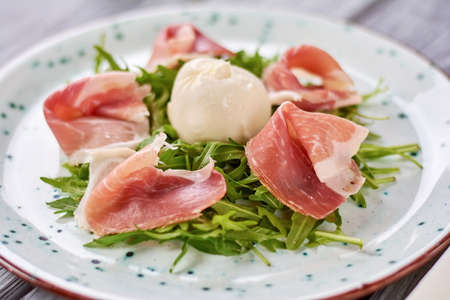 Delicatessen salad with burrata cheese. Delicious salad from arugula and meat at restaurant. Tasty dish on plate.の写真素材