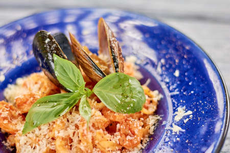 Appetizing pasta with mussels and basil. Delicious pasta frutti di mare close up. Pasta with seafood and red sauce. Delicious dinner on plate.の写真素材