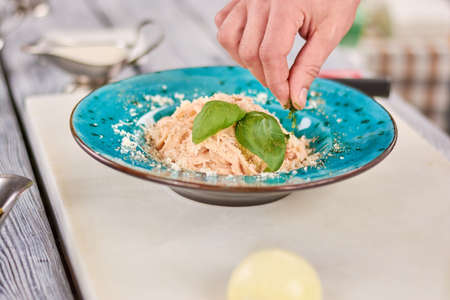 Delicious italian pasta with green basil. Chef hand serving appetizing pasta creama di pollo with cheese and greenery. Cooking and food preparing concept.の写真素材