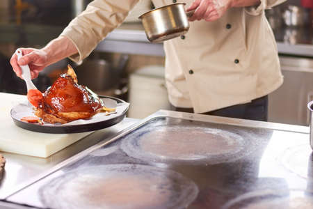 Chef processing lamb shank with sauce. Male chef at restaurant kitchen polishing with red sauce shank of lamb.の写真素材