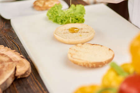 The process of cooking burger at kitchen. Bun for hamburger pouring with sauce. Cooking and culinary concept.の写真素材