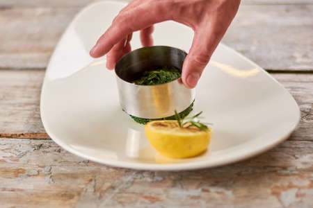 Chef hand forming a dish. Chef hand serving an appetizer with metl ring. Cook at work, kitchen.