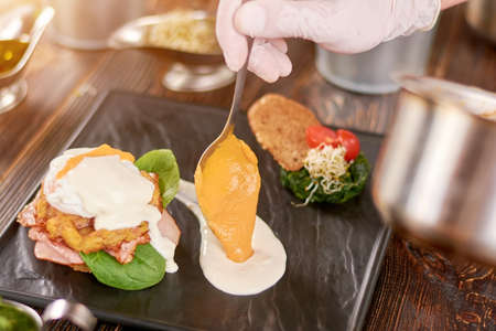 Cooking delicious benedict in restaurant. Chef hand serving tasty benedict with sauce. Food preparing and culinary.の写真素材