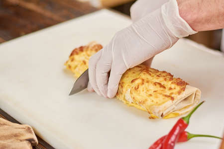 Chef hands cutting burrito on pieces. Cook chopping mexican burrito. Chef at work, cooking.の写真素材