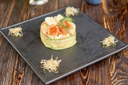Olivier salad with salmon and tobiko caviar. Appetizing olivier salad on plate in restaurant. Delicious dinner on black board.の写真素材