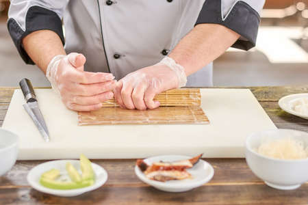 Chef hands shaping sushi roll. Male cook hands making japanese sushi roll with bamboo mat. Chef at work, kitchen.の写真素材