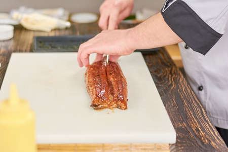 Chef hands slicing eel on cutting board. Male hands cutting fresh eel on white cutting board. Chef at work, kitchen.の写真素材