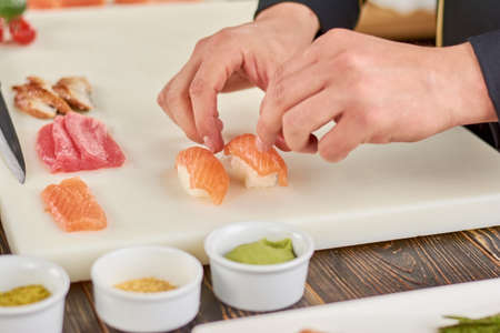 Chef hands cooking nigiri sushi. Male chef hands preparing nigiri sushi with salmon on white board. The process of sushi making.の写真素材