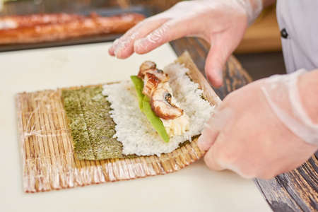 Cook hands making japanese sushi roll. The process of cooking sushi roll with eel, avocado, rice and nori. Preparing of roll unagi furay.の写真素材