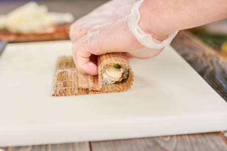 Cook in disposable gloves making sushi roll. Chef hands making long sushi roll. Famous japanese food.の写真素材