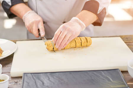 Cook in gloves cutting sushi roll in pieces. Chef sliced japanese sushi roll on cutting board. Chef...