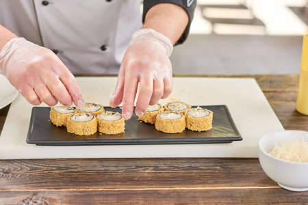 Chef hands putting sushi on plate. Cook in gloves placing delicious sushi rolls on black plate.の写真素材