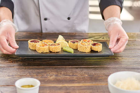 Chef hands holding plate with sushi rolls. Unagi sushi rolls on traditional japanese dish in cook...