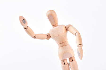 Wooden dummy showing greeting sign. Wooden figurine raised its hand over white background. Body language and gestures.の写真素材