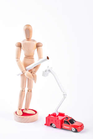 Wooden mannequin with tobacco cigarette. Human wooden dummy with cigarette, red fire truck on white background. The abuse of smoking leads to a fire.の写真素材