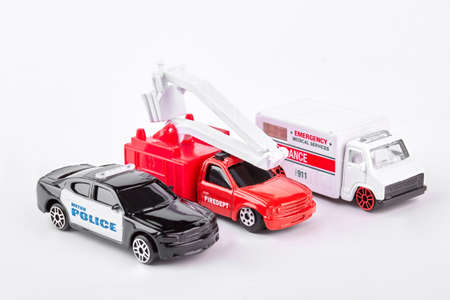 Close up of a toy ambulance with a fire engine and a police car on white background.