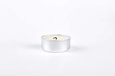 Tea candle with burned wick. Small white wax candle in circle metal base, isolated on white background.の写真素材