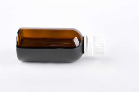 Glass bottle with cough syrup. Glass medical bottle with medicine lying on white background. Health care and cold treatment concept.の写真素材