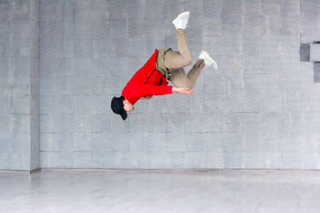 Rap dancer jumping on grey background. Portrait of a young male hip hop dancer jumping against grey background. Young rapper in high jump.の写真素材