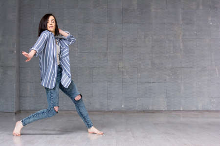 Young girl performing hip-hop dance. Young pretty woman dancing street dance on grey wall background.の写真素材
