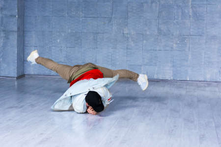 Yong modern style dancer in movement. Yong man in trendy clothes dancing brak dance on grey floor....