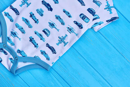 Detail of newborn organic bodysuit. White romper in transport print on blue wooden background close up. Infant boy cotton summer garment. Baby boy jumpsuit.の写真素材