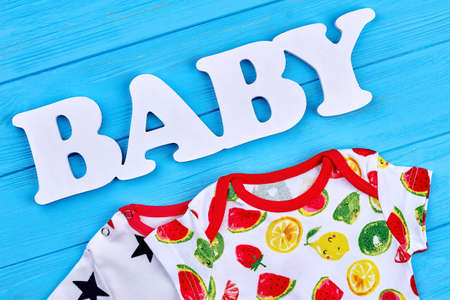 Fruit print cotton baby clothes. Close up of natural infant baby apparel, figure baby, blue wooden background.の写真素材