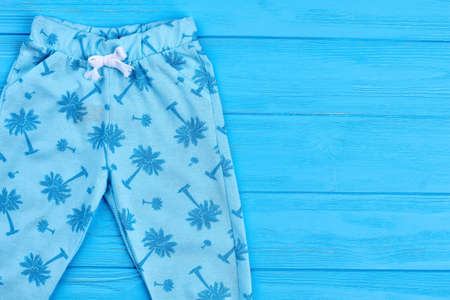 New fashion design baby leggings. Fashionable printed light blue pants for baby-girls, copy space. Modern trousers for little girls on blue wooden background.の写真素材