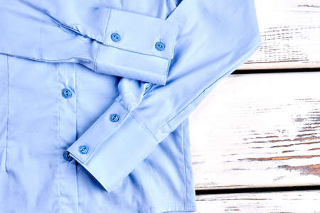 Detail of light blue cotton shirt. Long sleeve blue blouse on wooden background close up. Formal outfit on sale.の写真素材