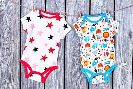 Infants clean apparel hanging on rope. Newborn kids printed bodysuits drying on clothesline on old wooden background.の写真素材