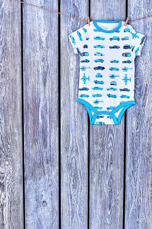 Boys patterned bodysuit hanging on rope. Baby boy soft romper drying on clothesline on wooden background, copy space.の写真素材