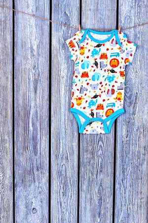 Infant girl bodysuit hanging on rope. Clothesline with drying kids summer romper on old wooden...