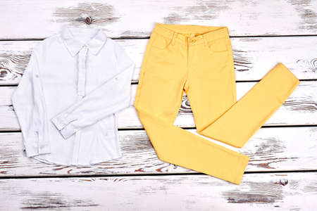 Girls blouse and yellow trousers. Teen girl white cotton shirt, colored pants on white wooden background. Young lady boutique apparel.の写真素材